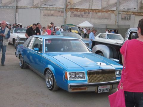 1991 Ford Crown Victoria - A crowd gathers around a custom blue Buick Regal at an outdoor car show.