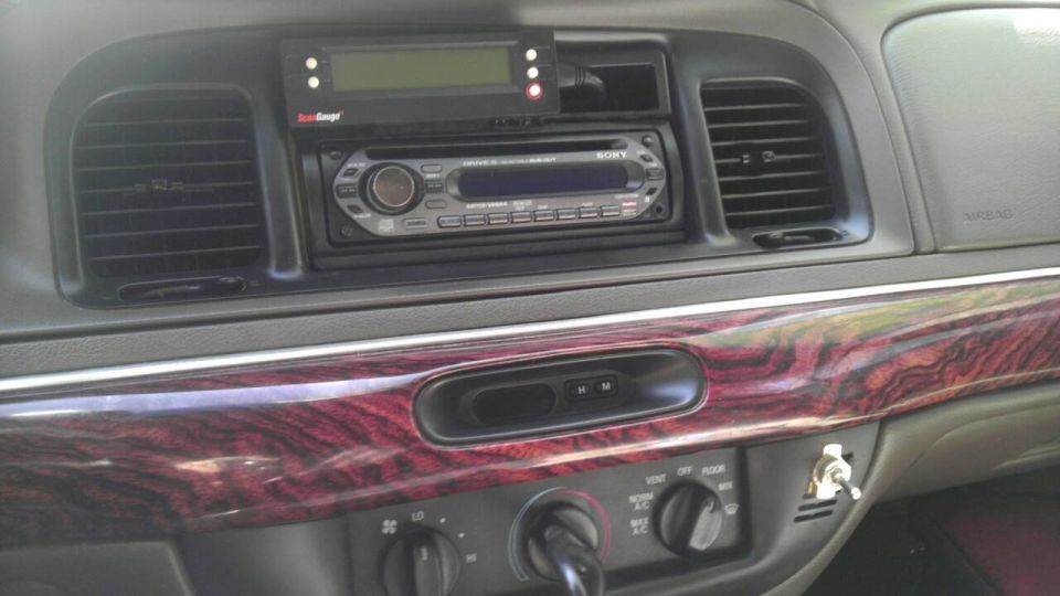 Car dashboard with Sony stereo, air vents, and wood trim. Aftermarket gauge above stereo