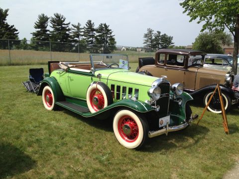 1988 Ford Bronco - Two vintage cars, a green convertible and a brown coupe, are displayed outdoors on a grassy field.
