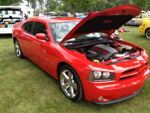 1988 Ford Bronco - A red Dodge Charger is displayed with its hood open, revealing the HEMI engine, at an outdoor car show.