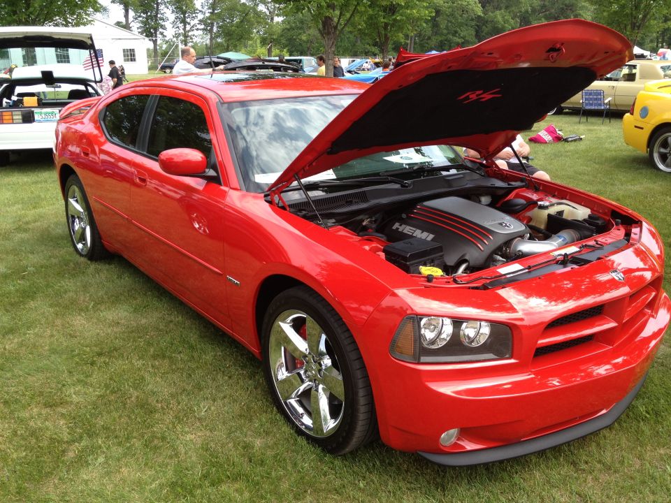 Red Dodge Charger, hood up showing HEMI engine. Parked on grass with other cars and people around