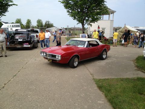 1988 Ford Bronco - A red convertible is parked at an outdoor event with other vehicles and people in the background.
