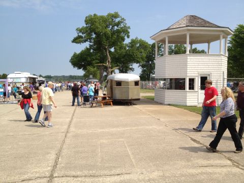 1988 Ford Bronco - People mill about at an outdoor event, with trailers and a small building visible.