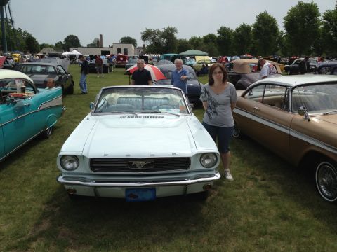 1988 Ford Bronco - A woman stands next to a light blue convertible at an outdoor car show with other vehicles in the background.