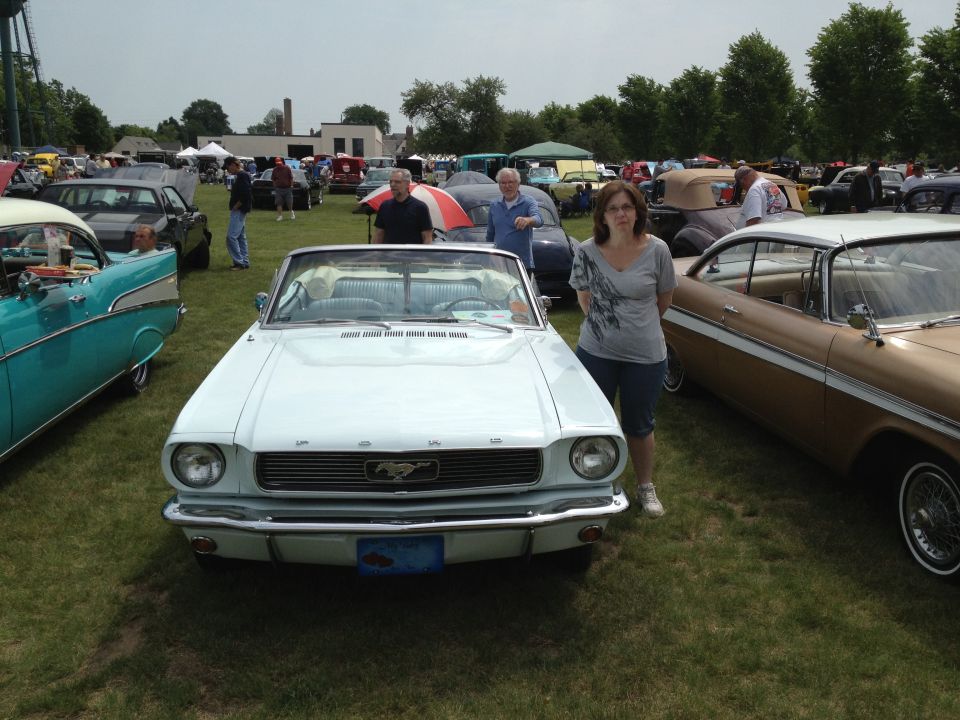Light blue convertible Mustang with a woman standing next to it at a car show