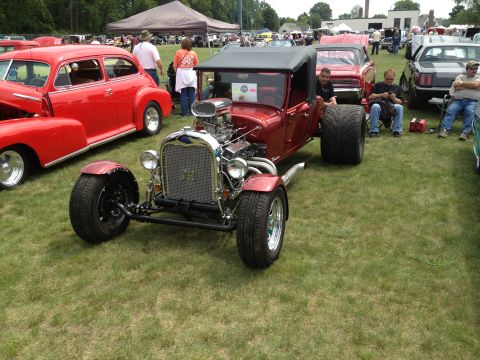 1988 Ford Bronco - A custom red hot rod with a prominent engine sits on display at an outdoor car show.
