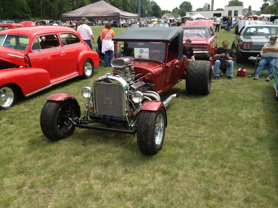 Red hot rod with exposed engine and large rear tires parked on grass