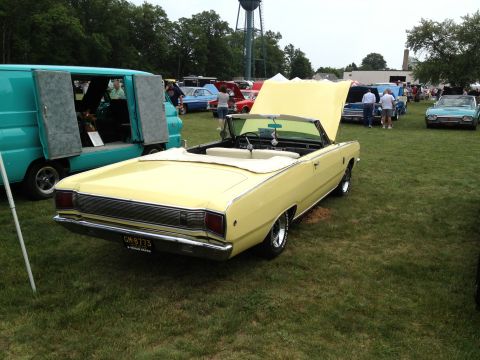 1988 Ford Bronco - A yellow convertible is parked on grass at a car show with other vehicles and a water tower in the background.