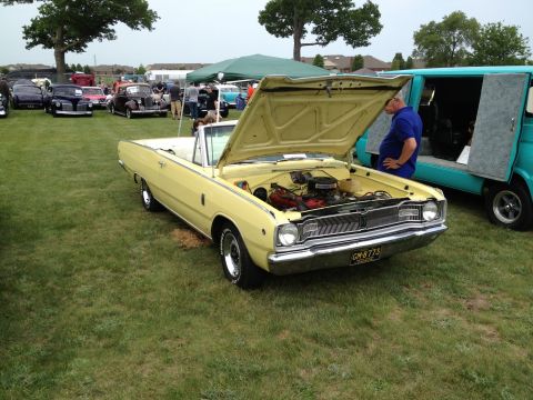 1988 Ford Bronco - A yellow convertible with its hood open is displayed on a grassy field next to a teal van. The license plate is visible.