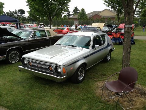 1988 Ford Bronco - A silver AMC Gremlin is parked on a grassy lawn at an outdoor car show, with several other vehicles visible.