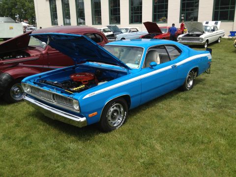 1988 Ford Bronco - A blue 1973 Plymouth Duster is displayed with its hood open at an outdoor car show.