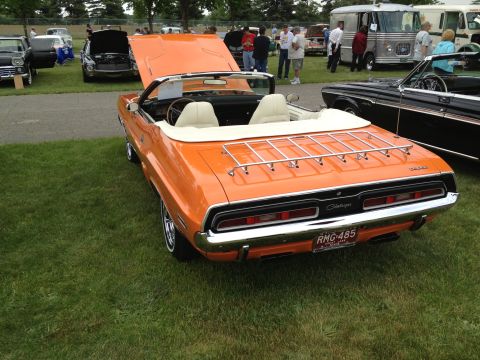 1988 Ford Bronco - An orange convertible with a luggage rack is parked on the grass at an outdoor car show.