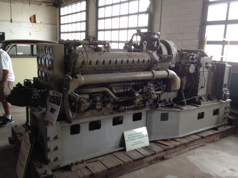 Packard diesel engine on wooden base, with informational signs and a person standing nearby