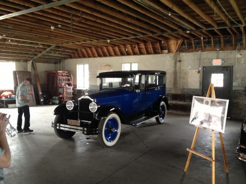 1988 Ford Bronco - A vintage blue sedan is displayed indoors with a man standing nearby and an easel with a picture.
