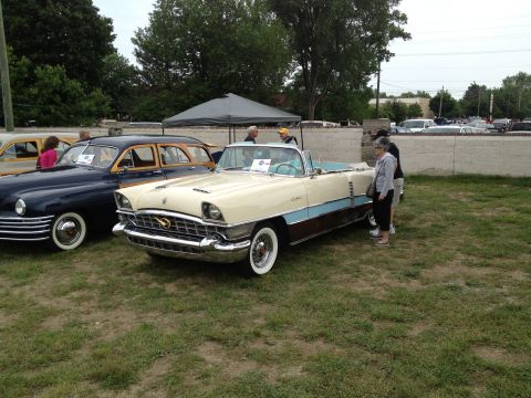 1988 Ford Bronco - A vintage Packard convertible is displayed at an outdoor car show next to a woody wagon.