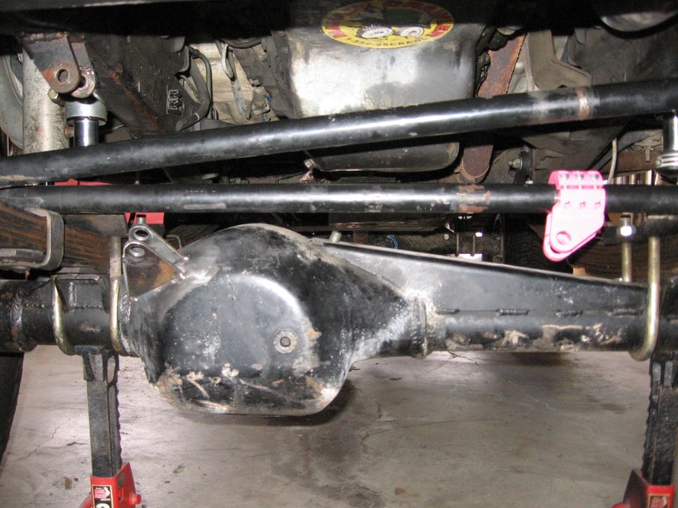 Underside view of vehicle's rear axle, leaf springs, and steering linkage. Vehicle is on jack stands