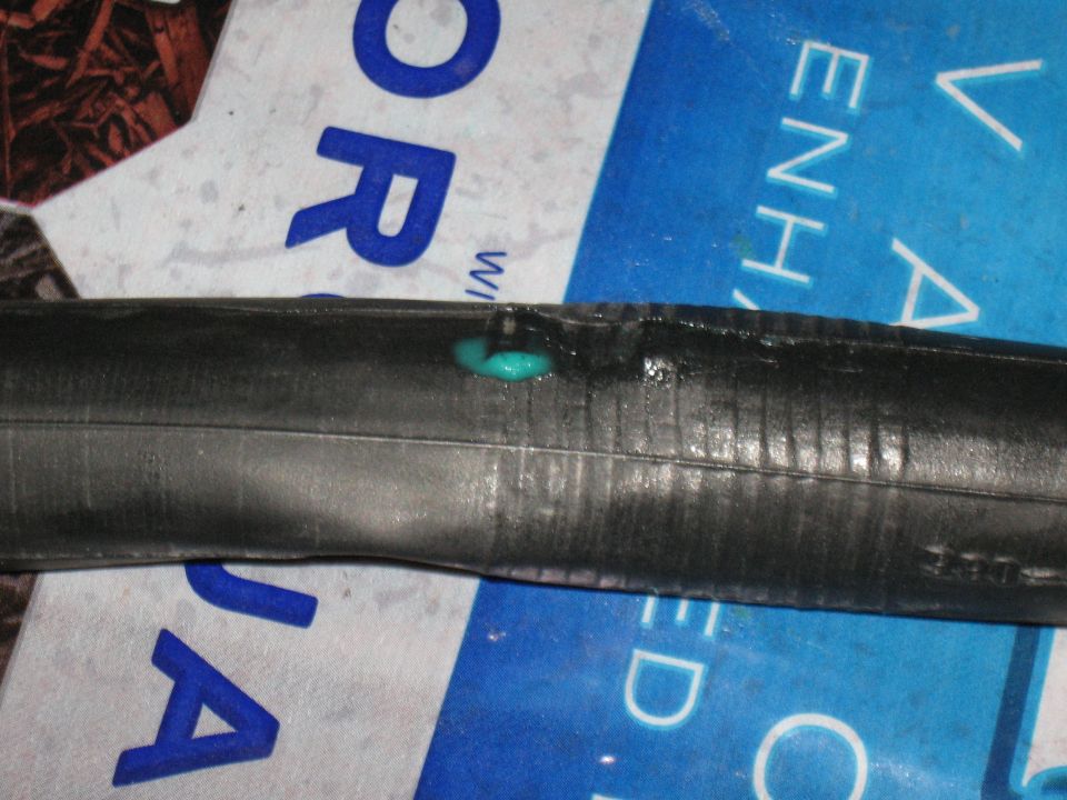 Bicycle inner tube with a turquoise sealant leak, showing ribbed texture and blue lettering on a white background