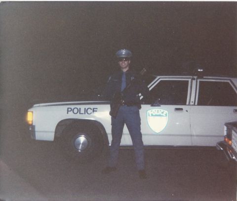 2001 Ford Crown Victoria - A police officer stands beside a marked patrol car at night.