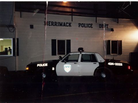 2001 Ford Crown Victoria - A police car is parked outside the Merrimack Police Department building at night.