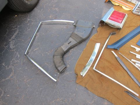 2001 Ford Crown Victoria - Various car parts, including a flexible duct and chrome trim, are laid out on a brown cloth on asphalt.