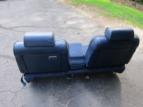 2001 Ford Crown Victoria - A detached blue car seat with headrests and an armrest is placed on a paved surface outdoors.