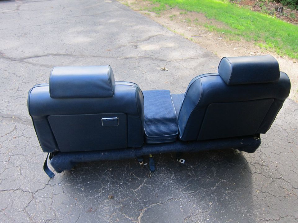 Blue car seat with headrests and armrest, sitting on cracked asphalt