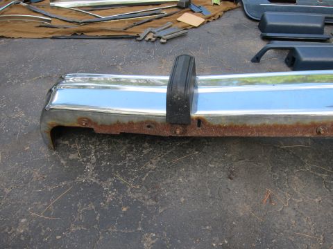 2001 Ford Crown Victoria - A detached chrome bumper with a black rubber bumperette shows signs of rust along its lower edge.