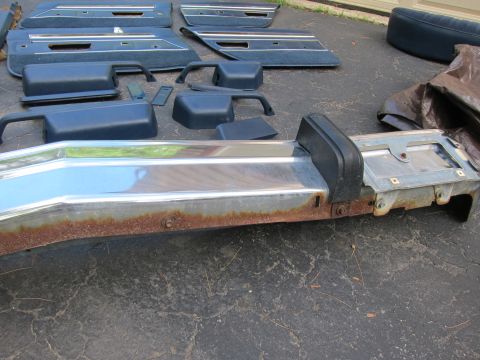 2001 Ford Crown Victoria - Disassembled parts including a chrome front bumper showing rust and several blue interior door panels are laid out on the ground.