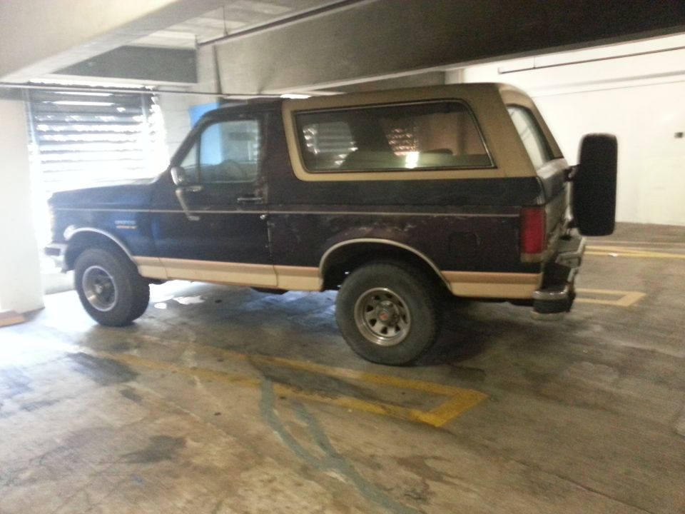 Dark brown and tan Ford Bronco parked in a garage, rear-mounted spare tire visible