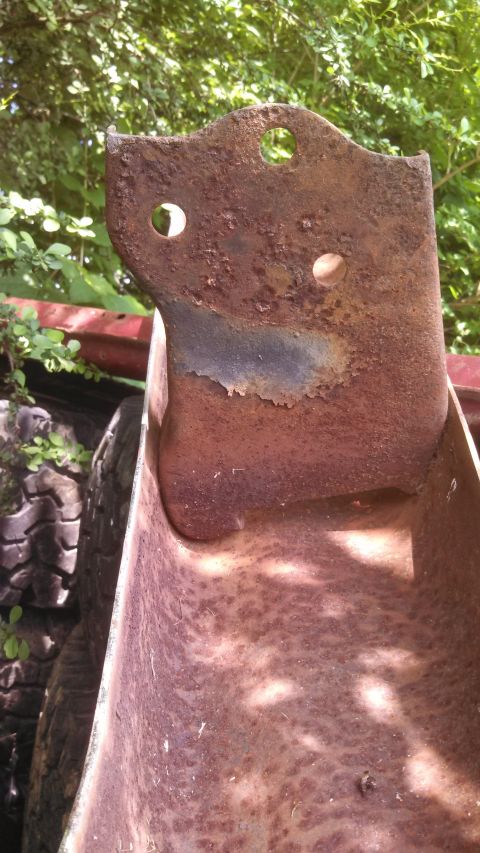 1979 Ford Bronco - A heavily rusted metal bracket with visible holes sits outdoors, partially obscured by greenery and a tire.