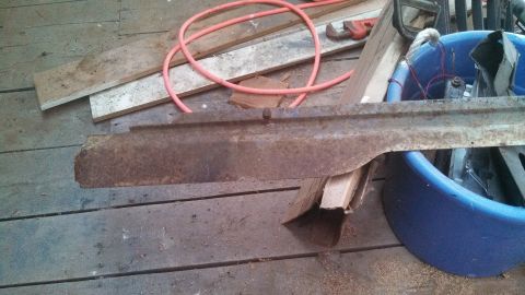 1979 Ford Bronco - A rusted metal part is shown on a wooden floor, with various tools and a blue tub in the background.