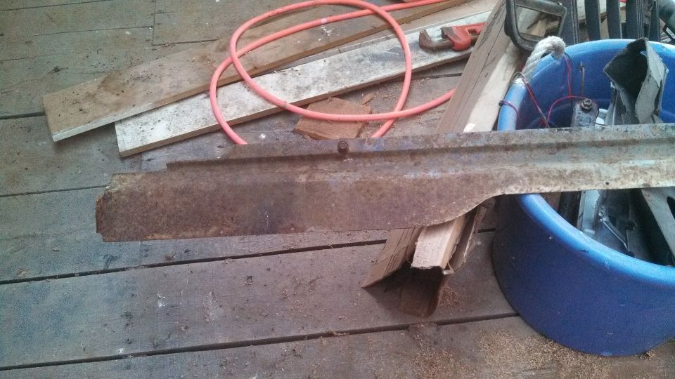 rusted metal piece with a curved edge, resting on a wooden floor next to a blue tub and orange hose