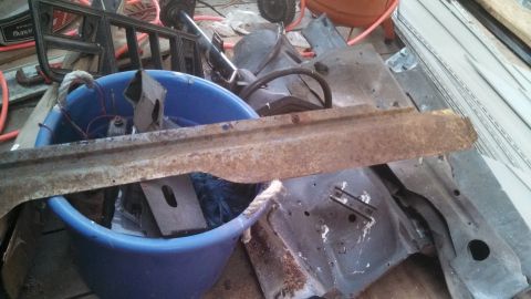 1979 Ford Bronco - Various rusty vehicle parts are piled up, including a long metal strip and pieces of body panels.