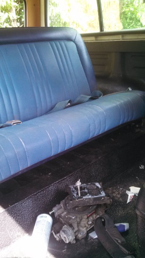 1979 Ford Bronco - The interior of a vehicle shows a blue bench seat and a carburetor on the floor.