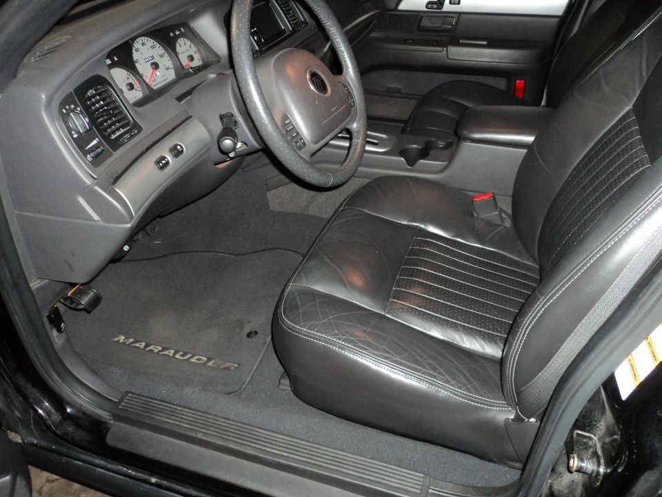 Interior of a 2004 Mercury Grand Marquis, showing the driver's seat, dashboard, and steering wheel. Floor mat says MARAUDER