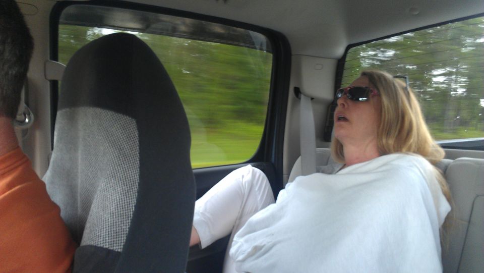 Woman sleeping in the back seat of a vehicle, with another passenger visible in the foreground