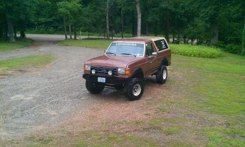 1987 Ford Bronco - This lifted 1987 Ford Bronco is parked on a gravel driveway surrounded by trees.