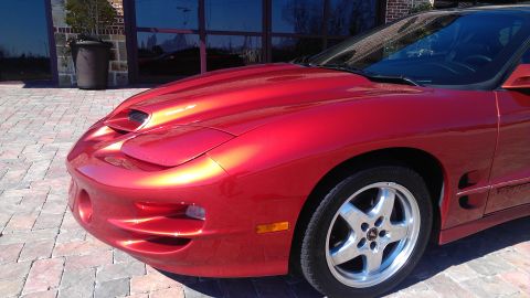 1980 Pontiac Trans Am - A red Pontiac Firebird is shown from the front quarter angle, parked on a brick paved area.