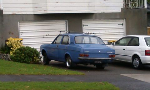 1969 Lincoln Continental - A blue sedan with a roof rack is parked in front of a garage, with a white hatchback beside it.