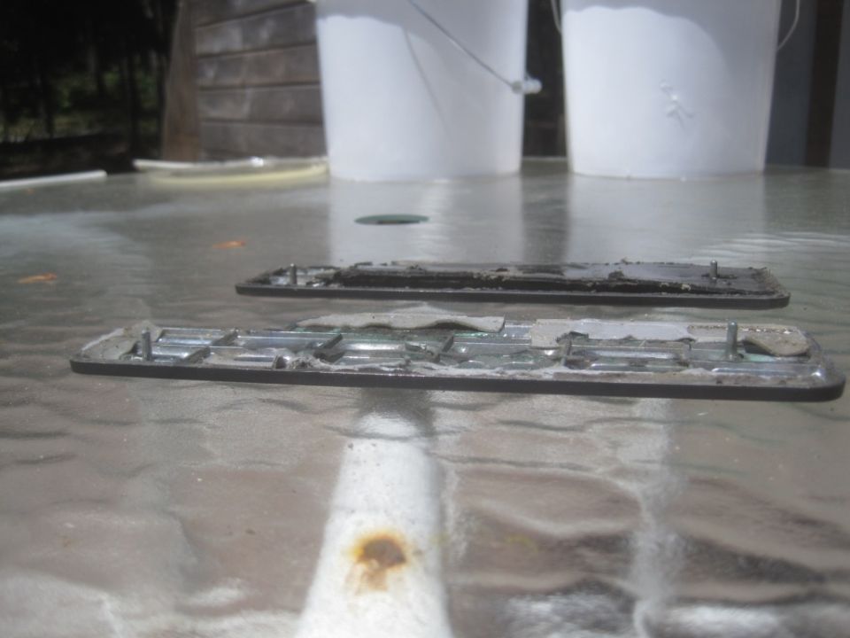 Two old, dirty car emblems with mounting pins on a glass table
