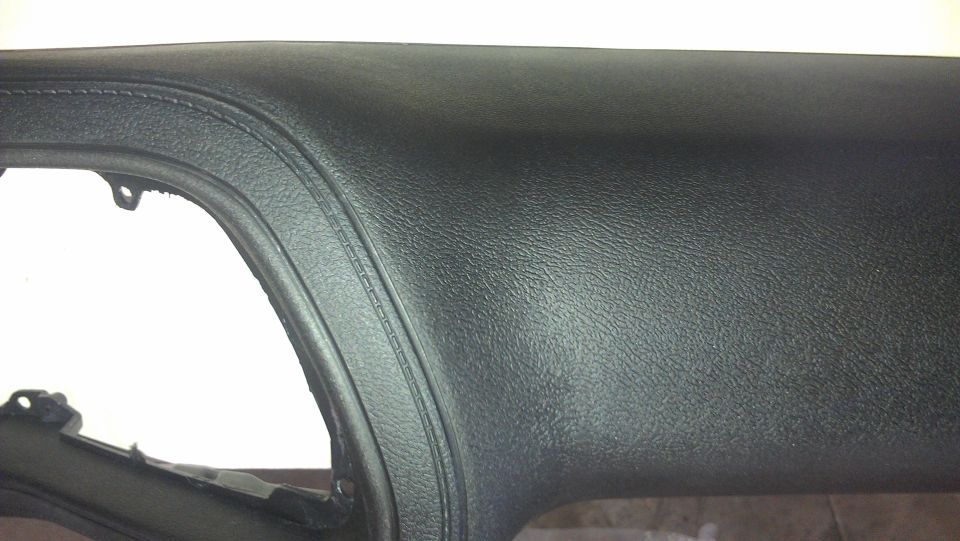 Close-up of a black textured dashboard with a curved seam. Part of a cutout is visible on the left