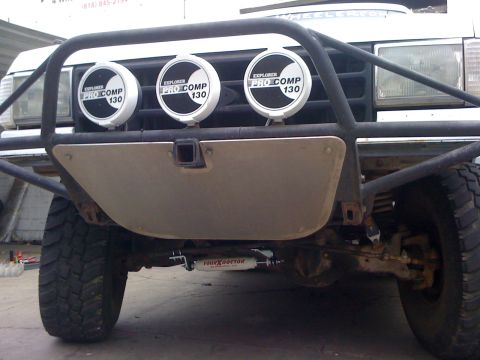 1990 Ford Bronco - Front of a vehicle with a tube bumper, metal skid plate and three Explorer Pro Comp 130 round driving lights.