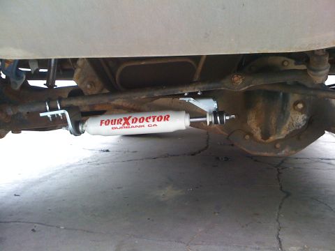 1990 Ford Bronco - white Four X Doctor (Burbank, CA) steering stabilizer mounted across the front axle underneath a vehicle.