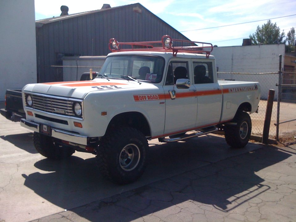 White International Harvester pickup with orange stripes and "OFF ROAD" text. It has a roof rack with lights and is lifted