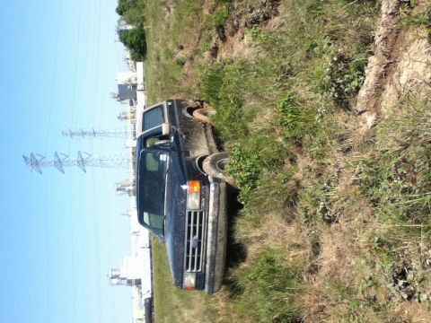 1988 Ford Bronco - A dark blue Ford F-Series truck is stuck in a grassy ditch, viewed from the front quarter angle.