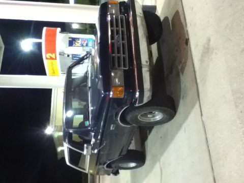1988 Ford Bronco - A dark blue Ford Bronco is parked at a gas station, illuminated by overhead lights.