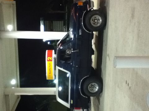 1988 Ford Bronco - A dark blue 1988 Ford Bronco with a white top is parked at a gas station at night.