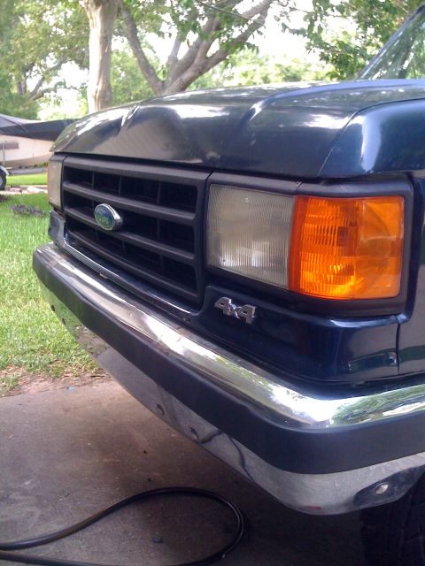 1988 Ford Bronco - Close-up of a dark blue Ford truck's front end, showing the grille, headlights, and chrome bumper.