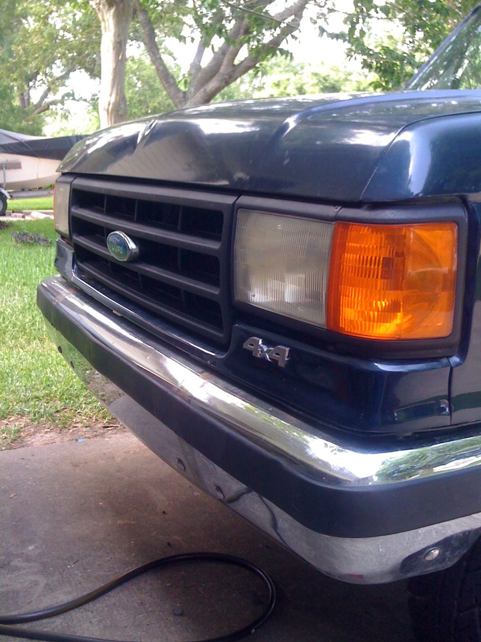 Dark blue Ford truck front grille with chrome bumper and 4x4 badge. Hood has a dent