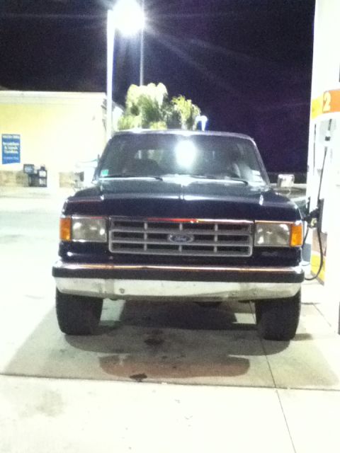 1988 Ford Bronco - This dark blue 1987 Ford Bronco is captured from the front at a gas station, likely during a nighttime fill-up.